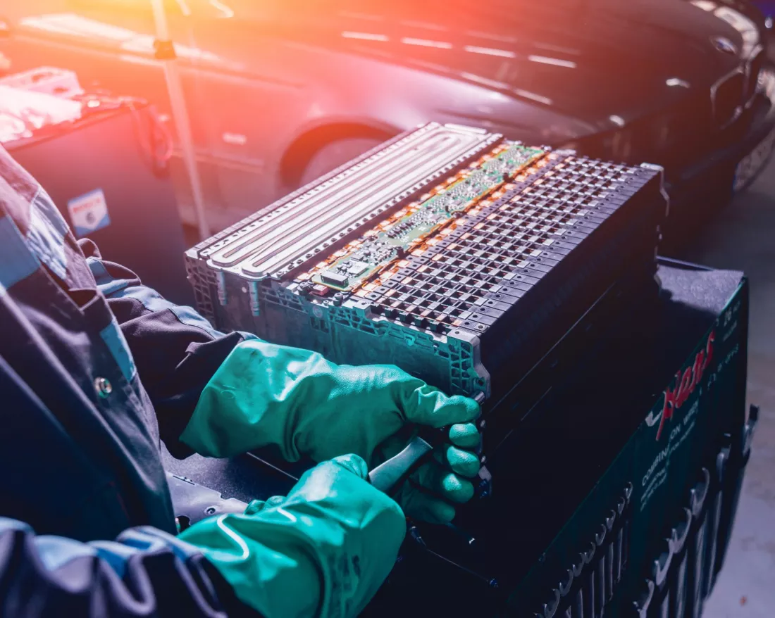 Gloved hands disassembling an electric car battery pack