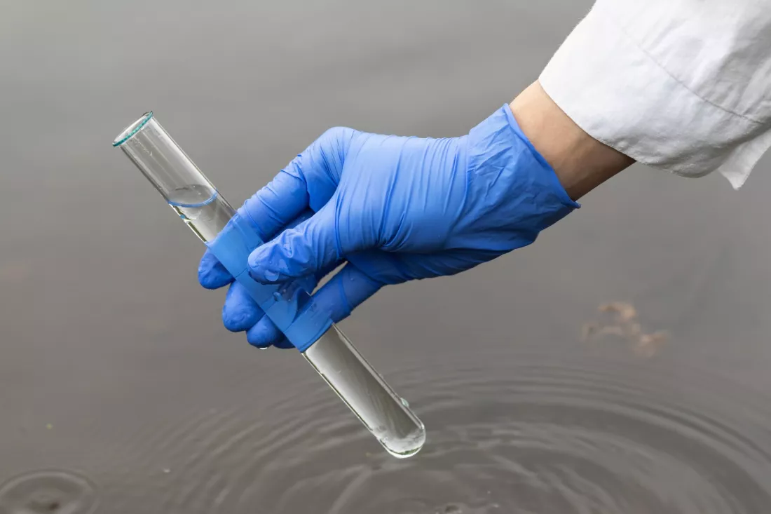 A gloved hand takes a river water sample into a test tube
