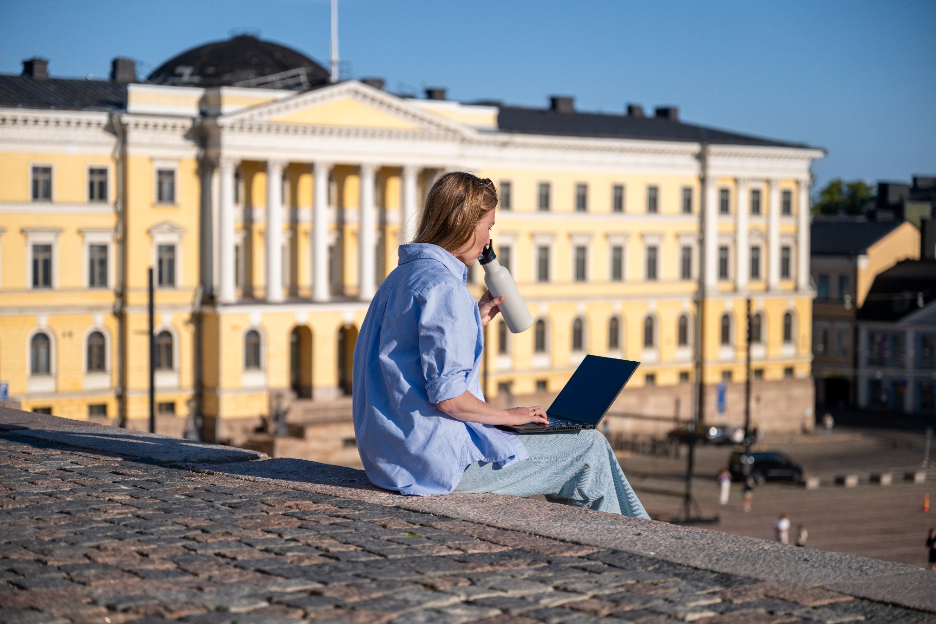 Young woman with a laptop sitting on the steps of Senate Square in Helsinki