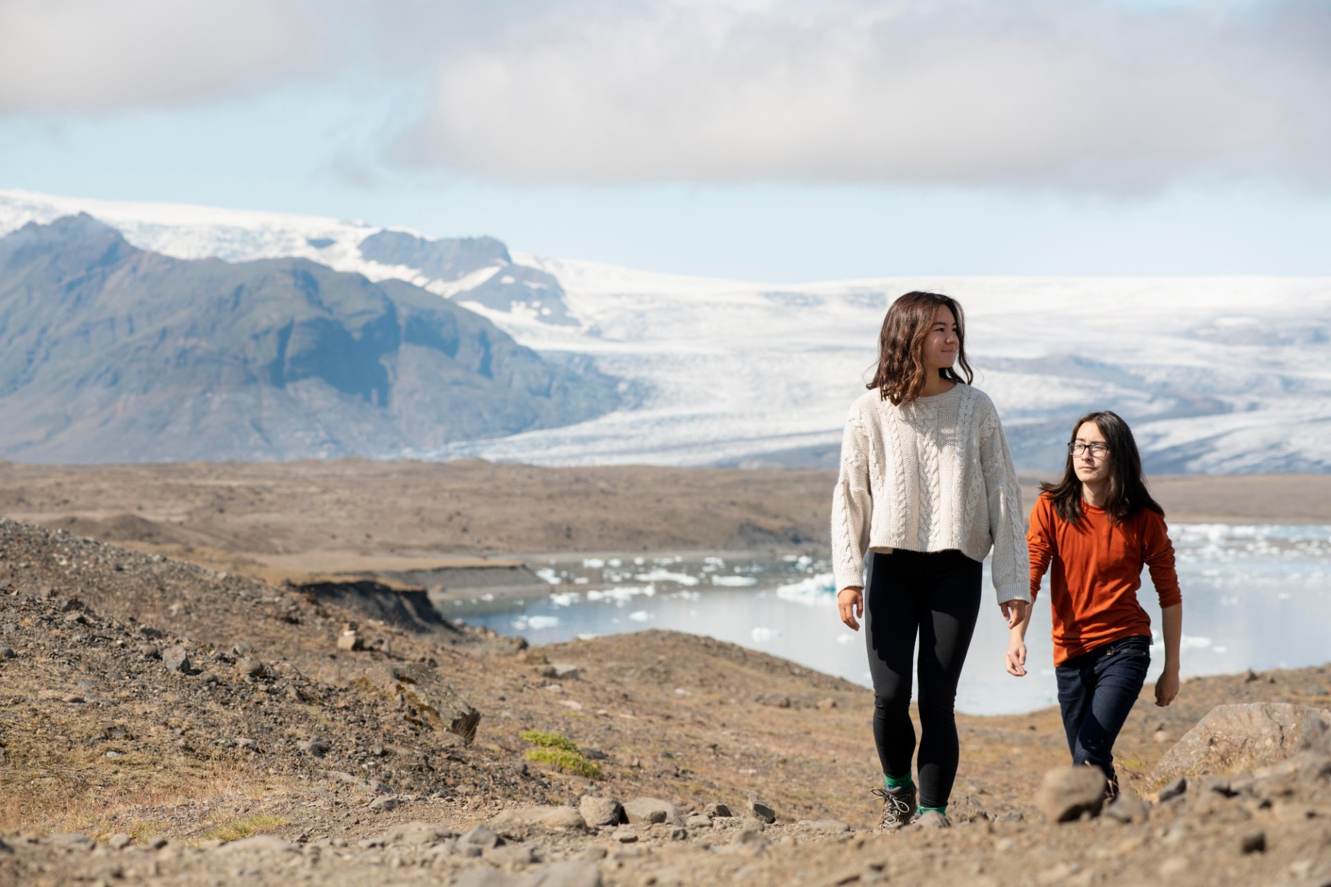 Two young women hiking in Iceland with a glacier and mountains behind them