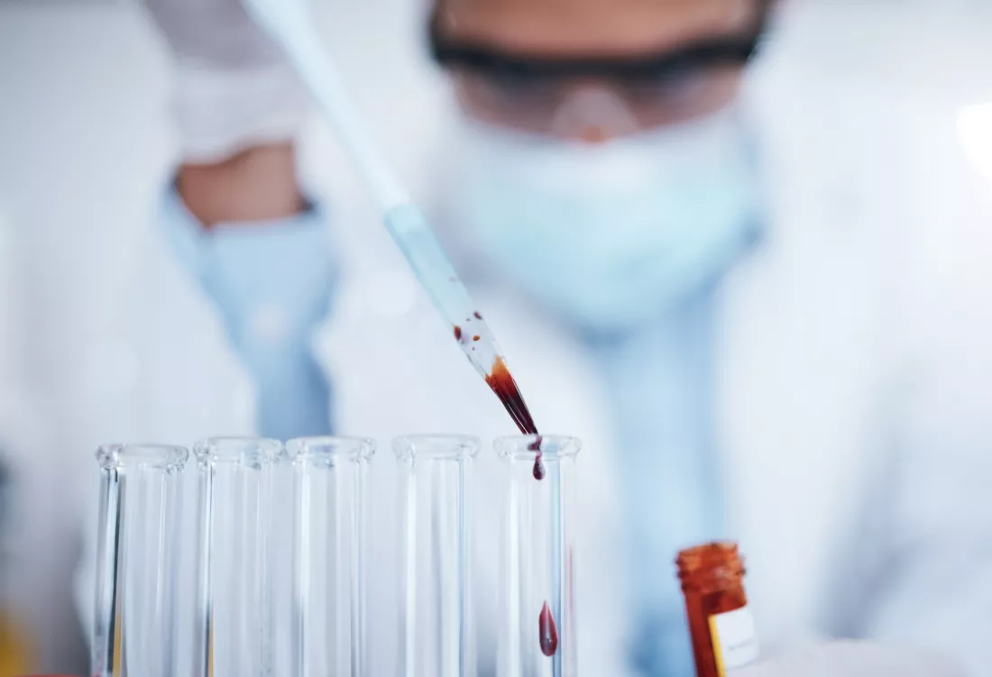 A researcher in a laboratory drips a blood sample into a test tube with a pipette.
